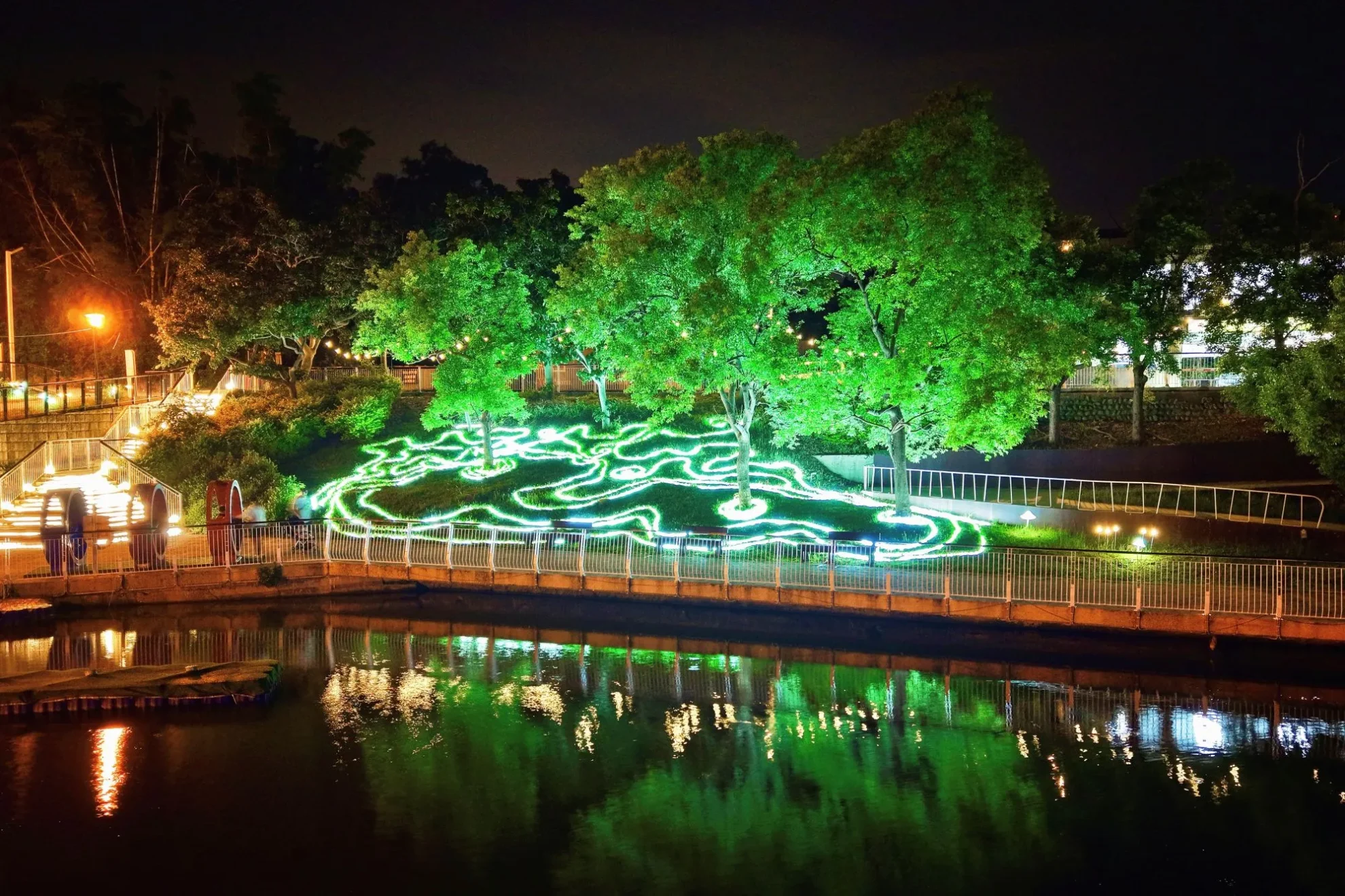 青草湖水岸樹林以綠色燈光及流線地景燈飾點亮,形成湖面倒影