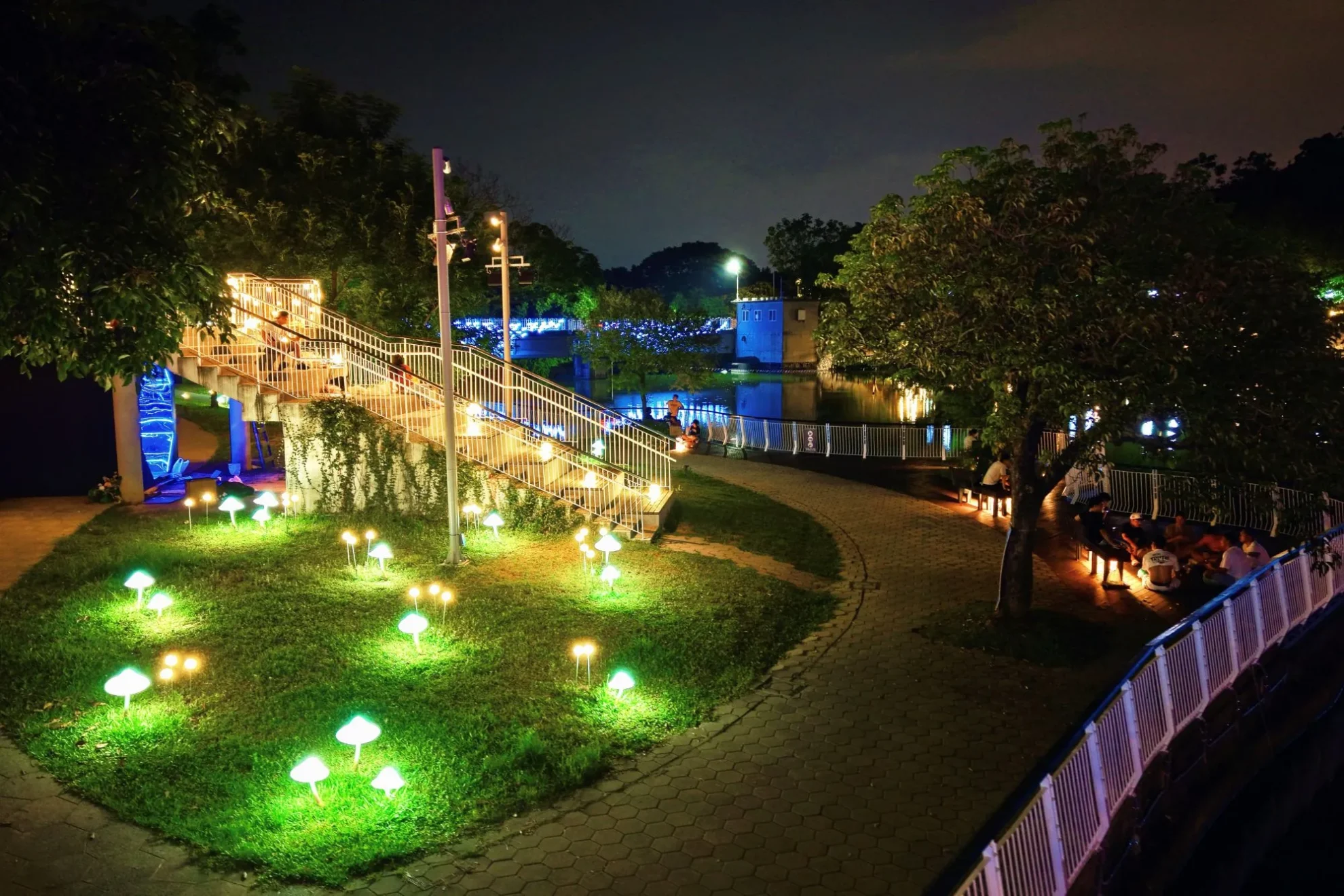 青草湖步道草地設置發光菇造型燈飾,遊客沿夜間水岸休憩